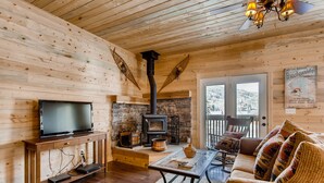 A cozy cabin interior with a wooden interior, a fireplace, a television on a wooden stand, and a sofa with patterned cushions.