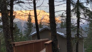 A wooden deck leading to a house surrounded by tall trees and mountains in the background. - Stunning, New 2 bedroom Unit Minutes from Alyeska Resort (Anchorage)