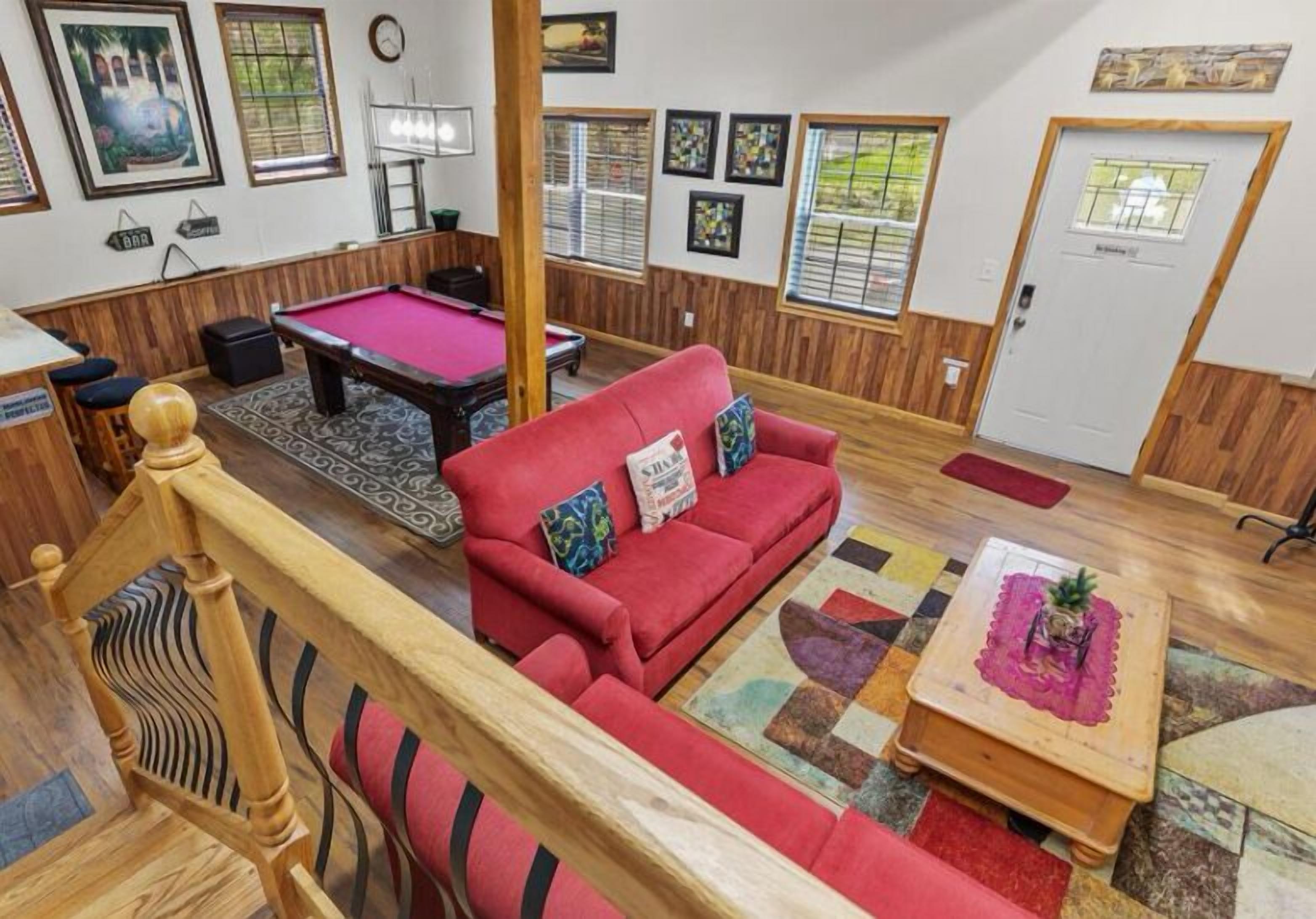 A cozy room with a pool table, red sofa, wooden flooring, and a staircase.