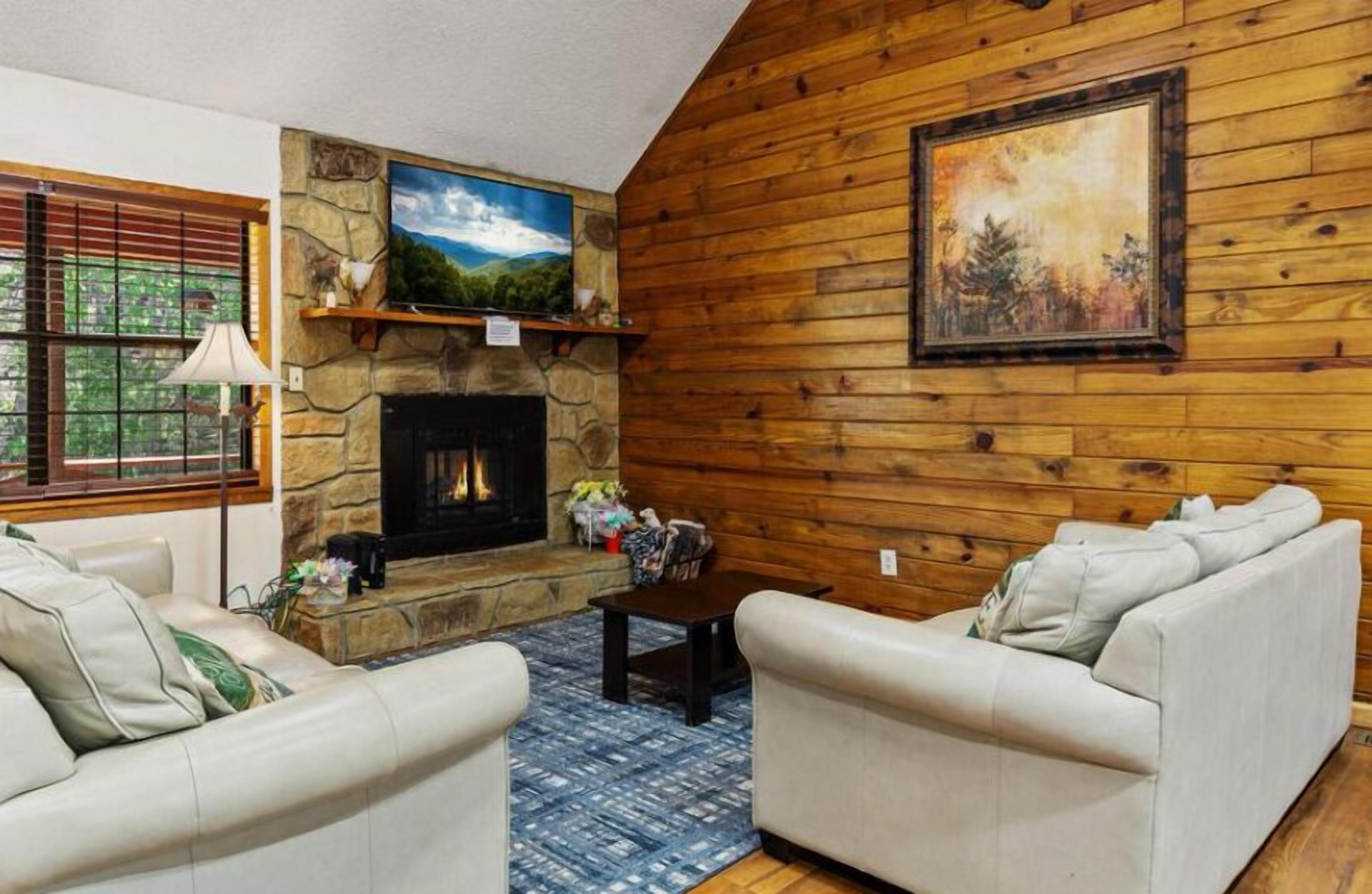 A cozy living room with a stone fireplace, wooden walls, and two white sofas.