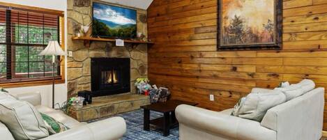 A cozy living room with a stone fireplace, wooden walls, and two white sofas.