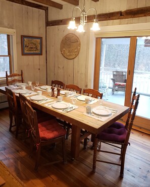 A wooden dining table set for six with chairs, a chandelier, and a view of a snowy landscape through a glass door.