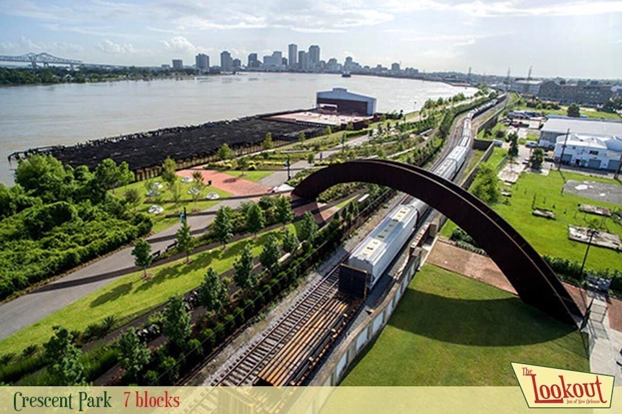 Ein Bahnhof mit einer markanten Bogenbrücke, Gleisen und umliegender Natur.