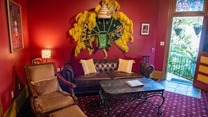 Una habitación con pared roja, un sofá con capitoné, una silla de madera, un tapete estampado y una mesa con un libro.