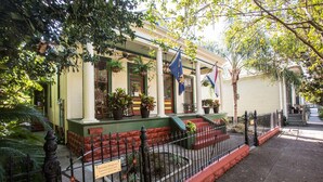 Un edificio histórico con un porche cubierto, plantas en macetas y banderas.