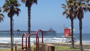 A playground with a slide and climbing structures, located near a beach with palm trees and a pier in the background. - Spacious ocean View Penthouse sleeps 8-10 w/large ocean facing deck! (Imperial Beach)