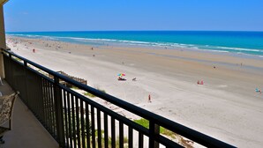 Blick auf einen Strand vom Balkon mit Geländer, feiner Sand und Meer.