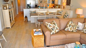 Ein gemütliches Wohnzimmer mit einer braunen Couch, einem Essbereich mit weißen Stühlen und einer Küche im Hintergrund.