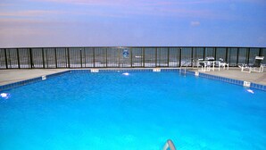 Ein Swimmingpool mit klarem, blauem Wasser, umgeben von einem schwarzen Zaun und Liegestühlen.