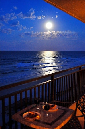 A balcony with a table set for two, overlooking the ocean at night with a visible moon and stars. - Premium Oceanfront Condo, Private Balcony & Beach, 130 straight 5 Star reviews (New Smyrna Beach)