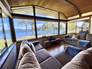 A modern living room with large windows offering a view of a lake and trees.