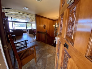 A wooden interior with a stone floor, a bench, a staircase, and a view of the outdoors through large windows.