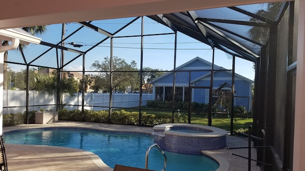 A covered outdoor swimming pool area with a hot tub, a chair, and a view of a residential neighborhood. - Olde Florida Style, 4 Bedrooms 3 Bath Pool\Hot Tub - Free Pool and Spa Heat! (Naples)