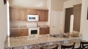 A kitchen with granite countertops, wooden cabinets, a microwave, an oven, and a sink. - Olde Florida Style, 4 Bedrooms 3 Bath Pool\Hot Tub - Free Pool and Spa Heat! (Naples)