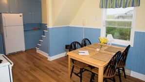A kitchen with blue cabinets, a wooden dining table with four chairs, and a window with blinds.