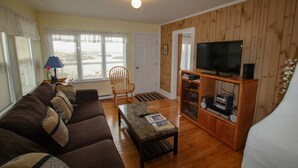 A living room with a brown sofa, a coffee table, a television on a wooden stand, and a window with blinds.