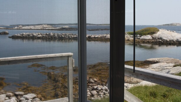 A coastal view through a window with a wooden deck and rocky shoreline.