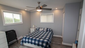 A bedroom with a bed, a ceiling fan, two windows, a nightstand, and a dresser.