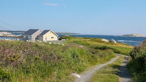 A coastal house with a gravel path leading to it, overlooking the sea.