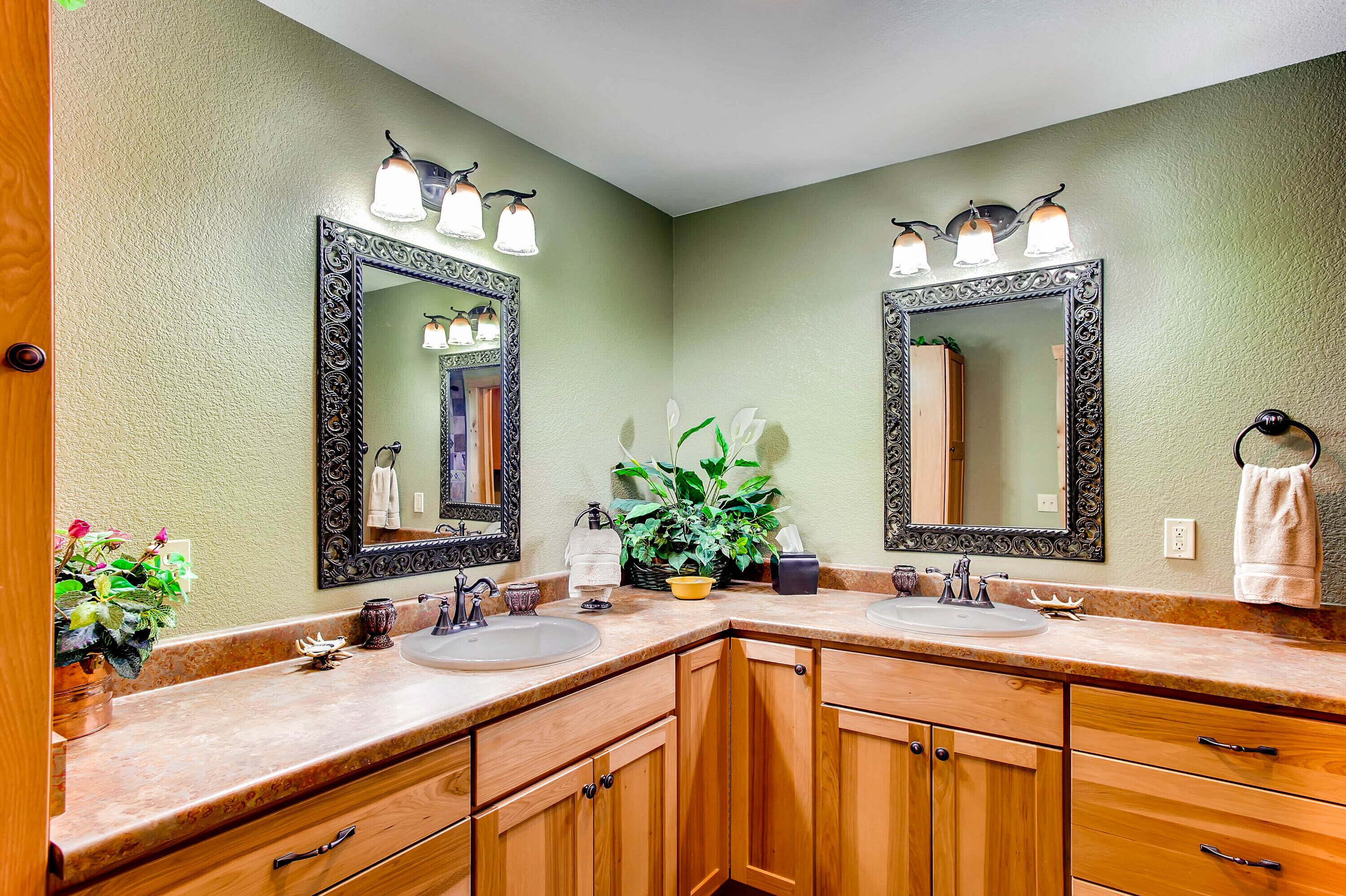 A bathroom with two sinks, wooden cabinets, a large mirror, and a potted plant.