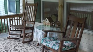 Une véranda avec deux fauteuils à bascule en bois, une petite table en verre et une nichoir.