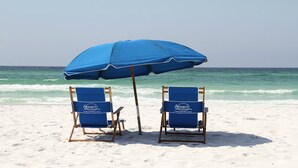 Twee strandstoelen met een blauwe parasol op een zandstrand.