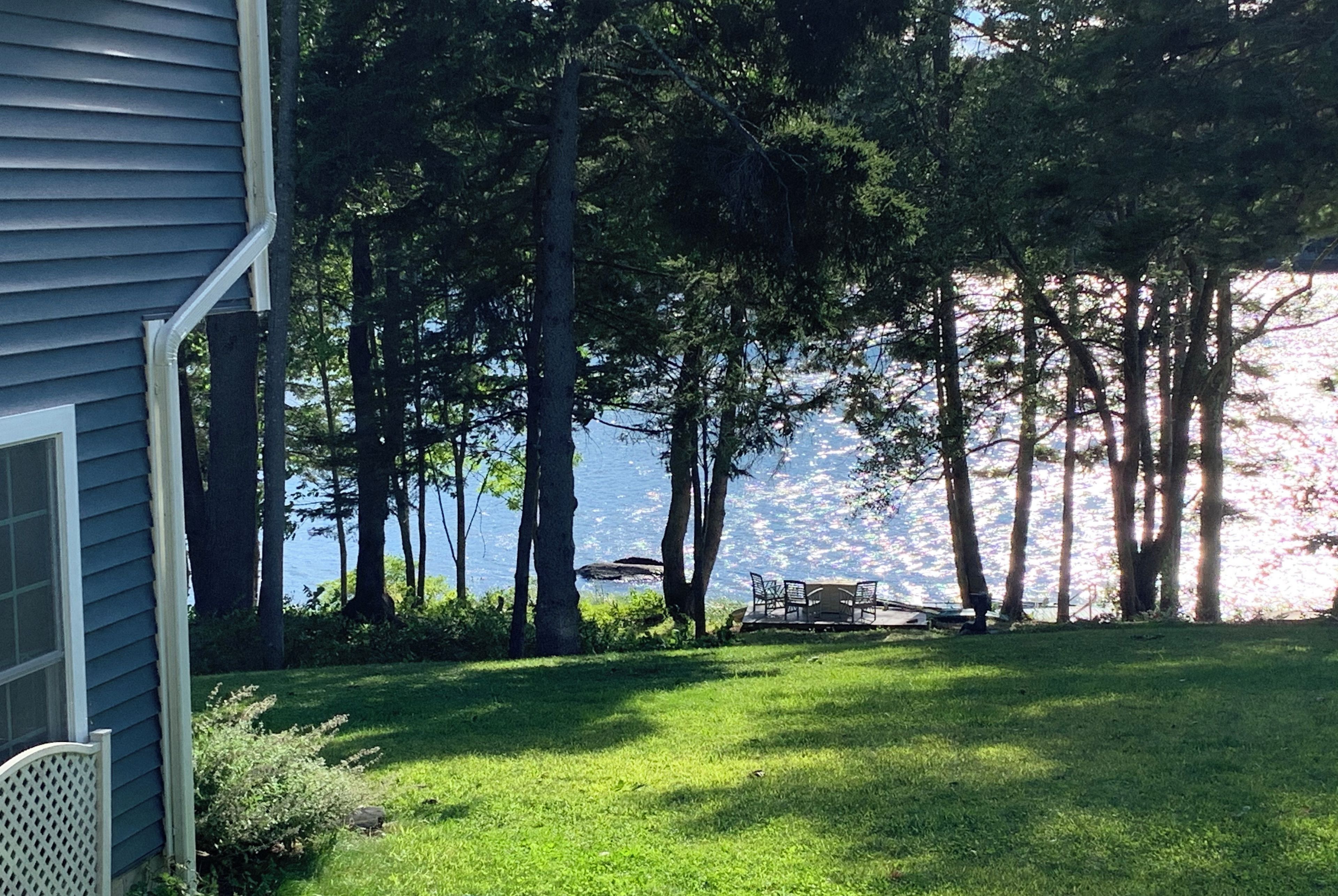 A house with a lawn and a dock extending into a lake, surrounded by tall trees.