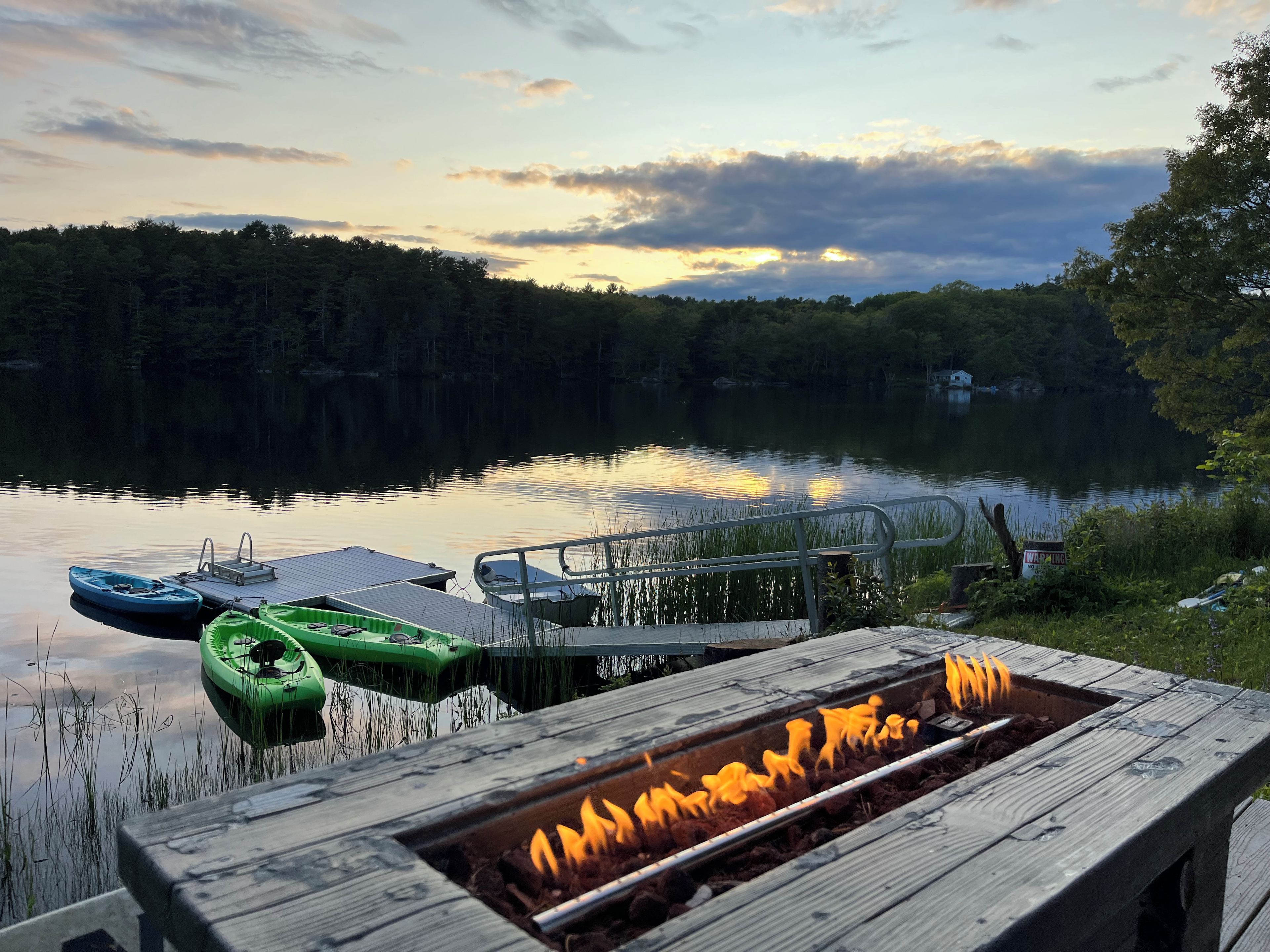 Terraza junto al lago con un brasero, barcos amarrados y barandilla de madera.