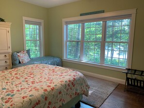Une chambre avec un grand lit, deux fenêtres, une commode et une chaise.