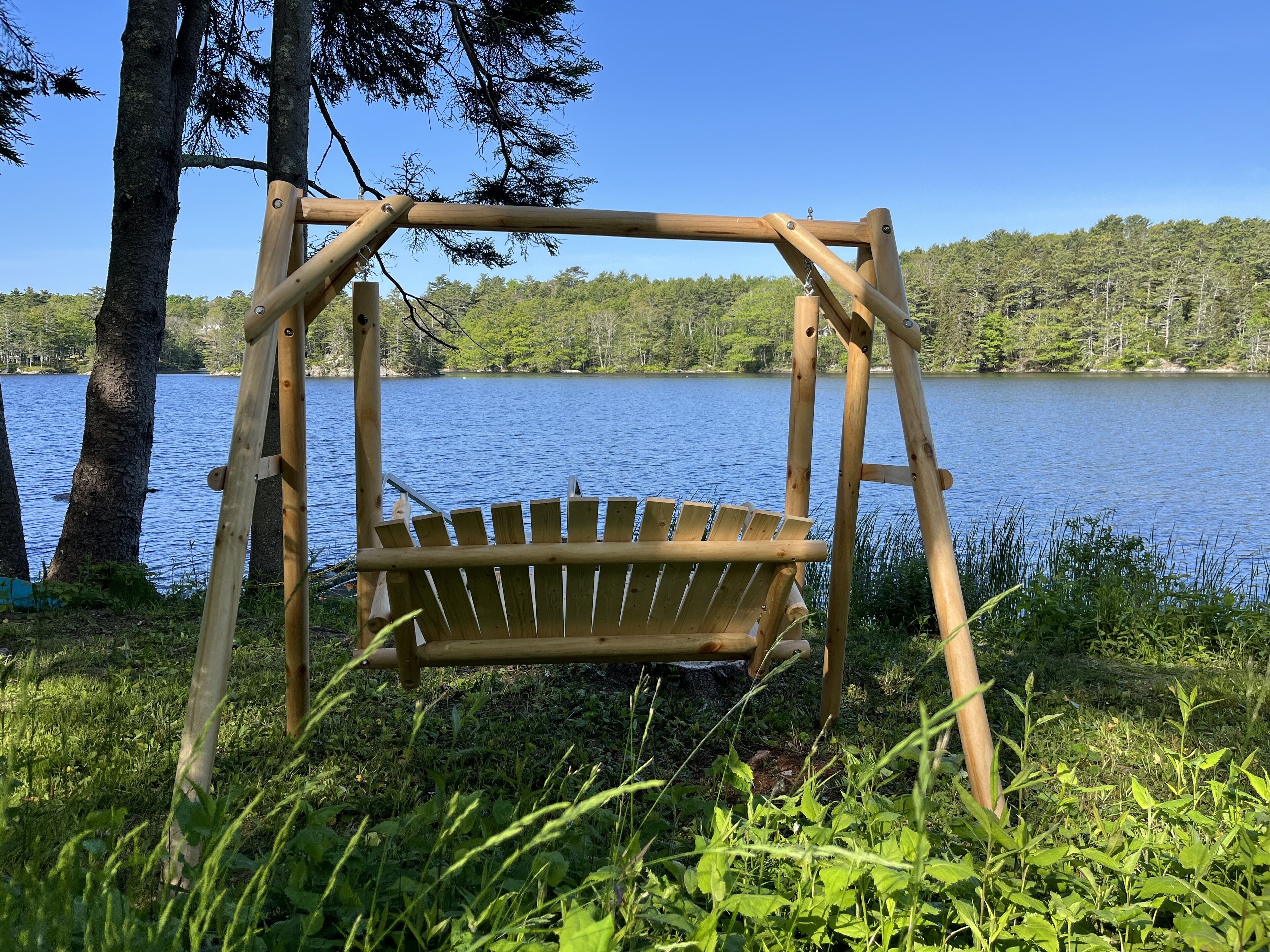 A wooden swing chair by a lake with a clear view of the water and trees.