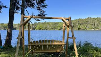 A wooden swing chair by a lake with a clear view of the water and trees.