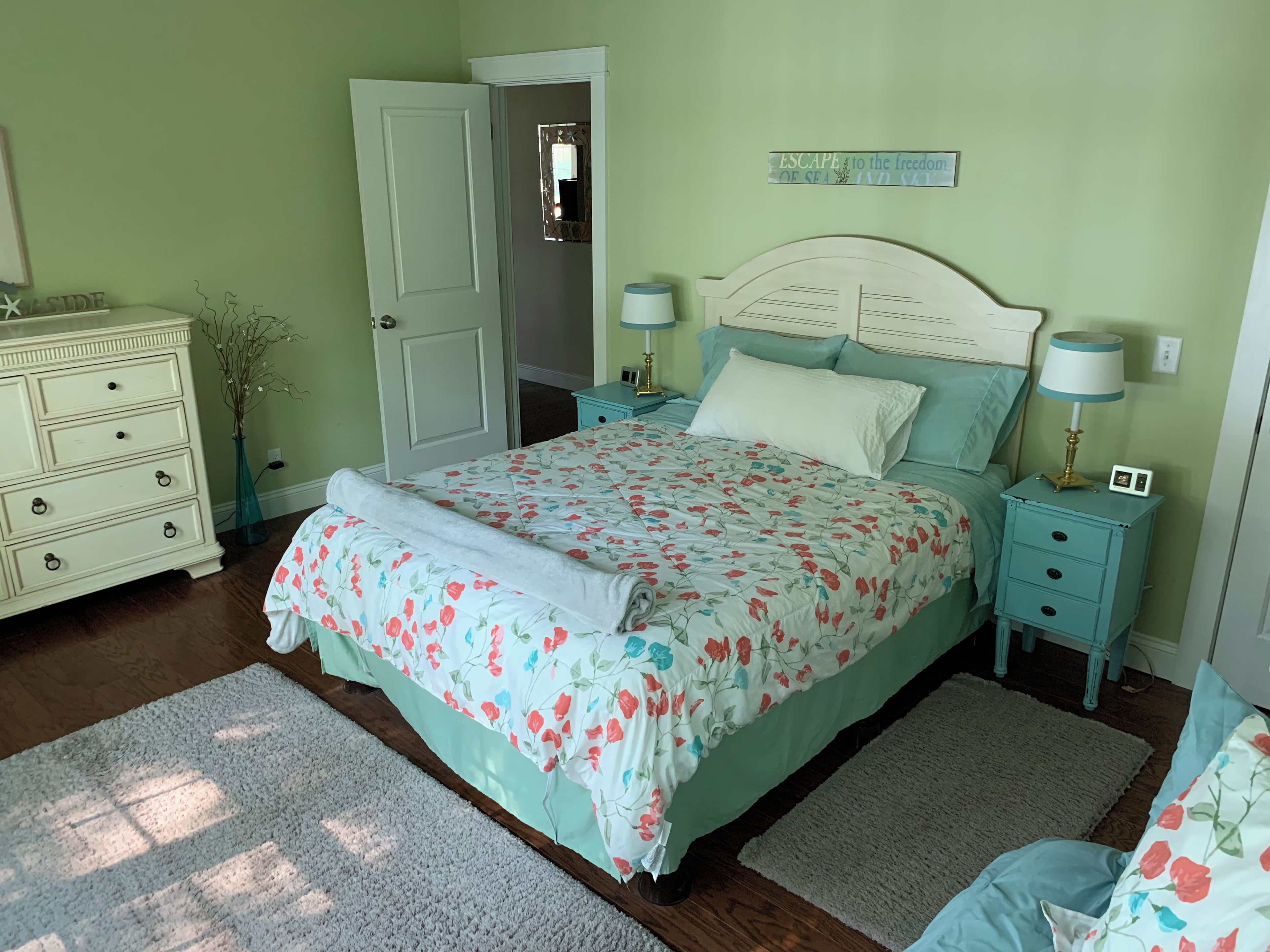 A bedroom with a bed, two bedside tables, a dresser, a mirror, and a door.