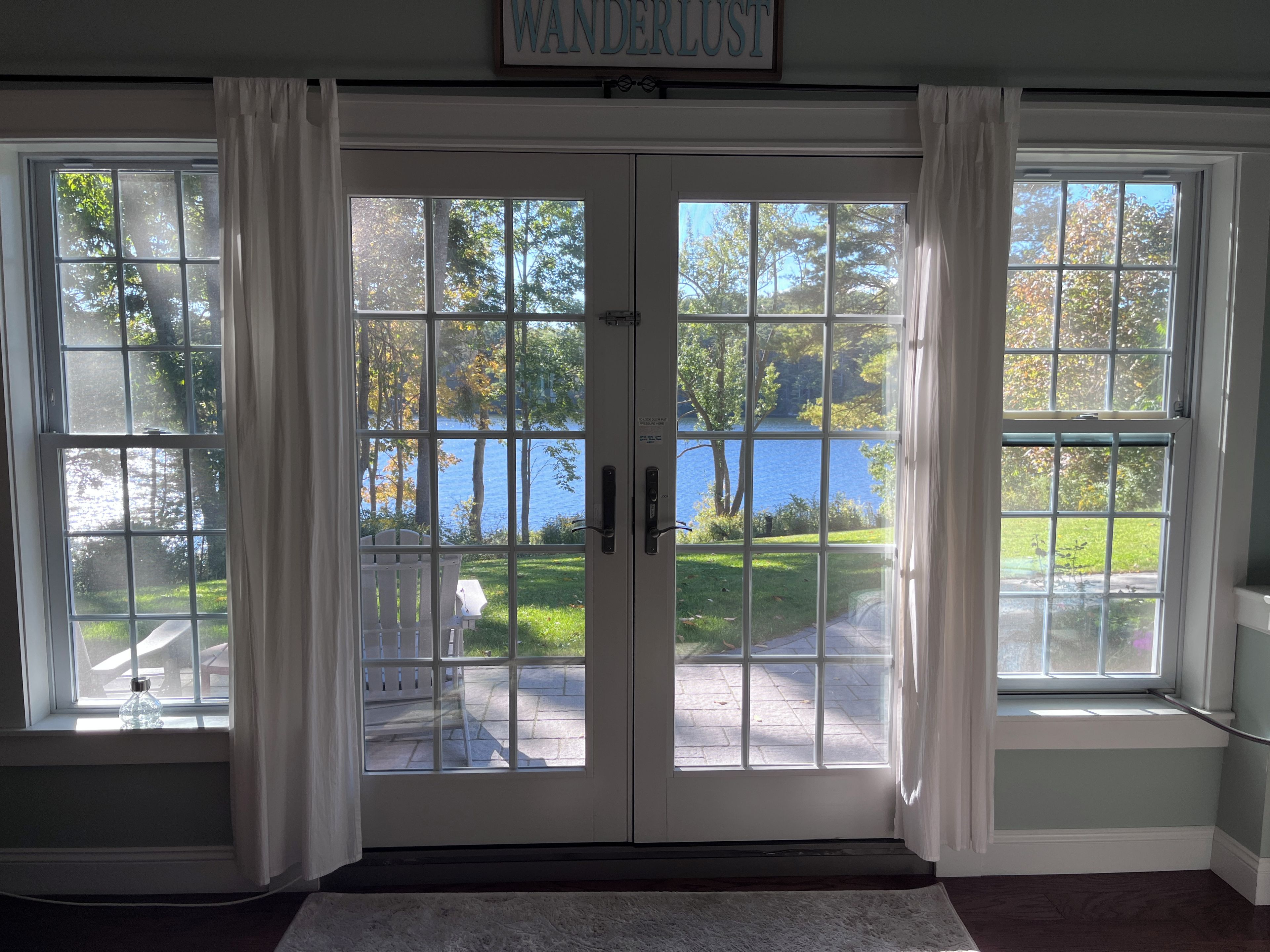 A double door entrance with a view of a lake and trees, a white rug on the floor, and a sign above the door.