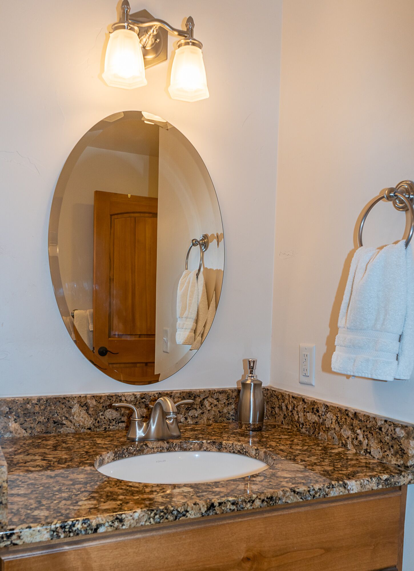 A bathroom with a granite countertop, a white sink, a round mirror, and two wall-mounted lights.