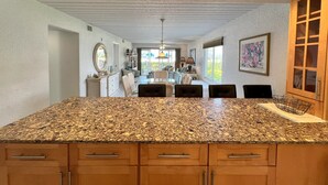 Una cocina con encimeras de granito, armarios de madera y un comedor con sillas y una mesa.