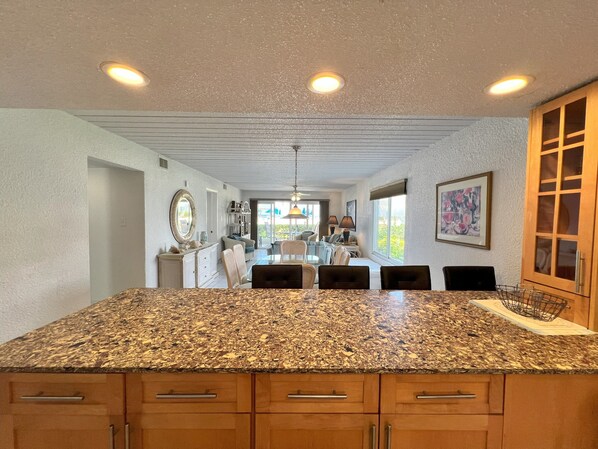 A kitchen with granite countertops, wooden cabinets, and a dining area with chairs and a table.