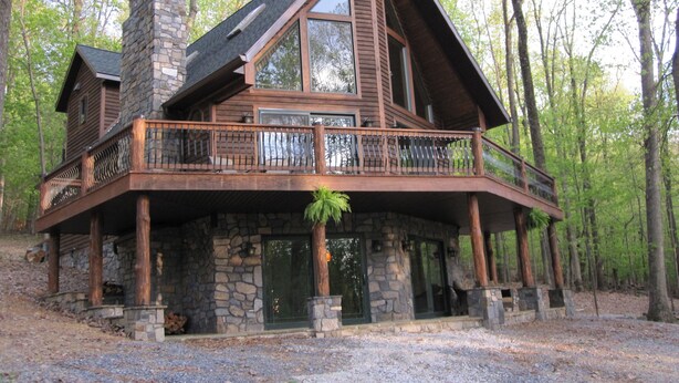 A large log cabin with a stone chimney, a balcony with a railing, and a stone foundation. - Luxury Cabin Nestled In The Beautiful Blue Ridge Mountains (Boonsboro)