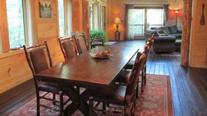 A wooden dining room with a large table and chairs, a chandelier, and a view of a living area with a sofa and lamp. - Luxury Cabin Nestled In The Beautiful Blue Ridge Mountains (Boonsboro)