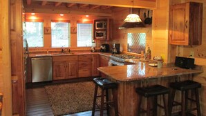 A wooden cabin kitchen with a central island, bar stools, a stove, and a microwave. - Luxury Cabin Nestled In The Beautiful Blue Ridge Mountains (Boonsboro)