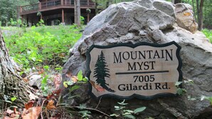 A large rock with a sign reading "Mountain Myst 7005 Gilardi Rd." in a forested area with a cabin in the background. - Luxury Cabin Nestled In The Beautiful Blue Ridge Mountains (Boonsboro)