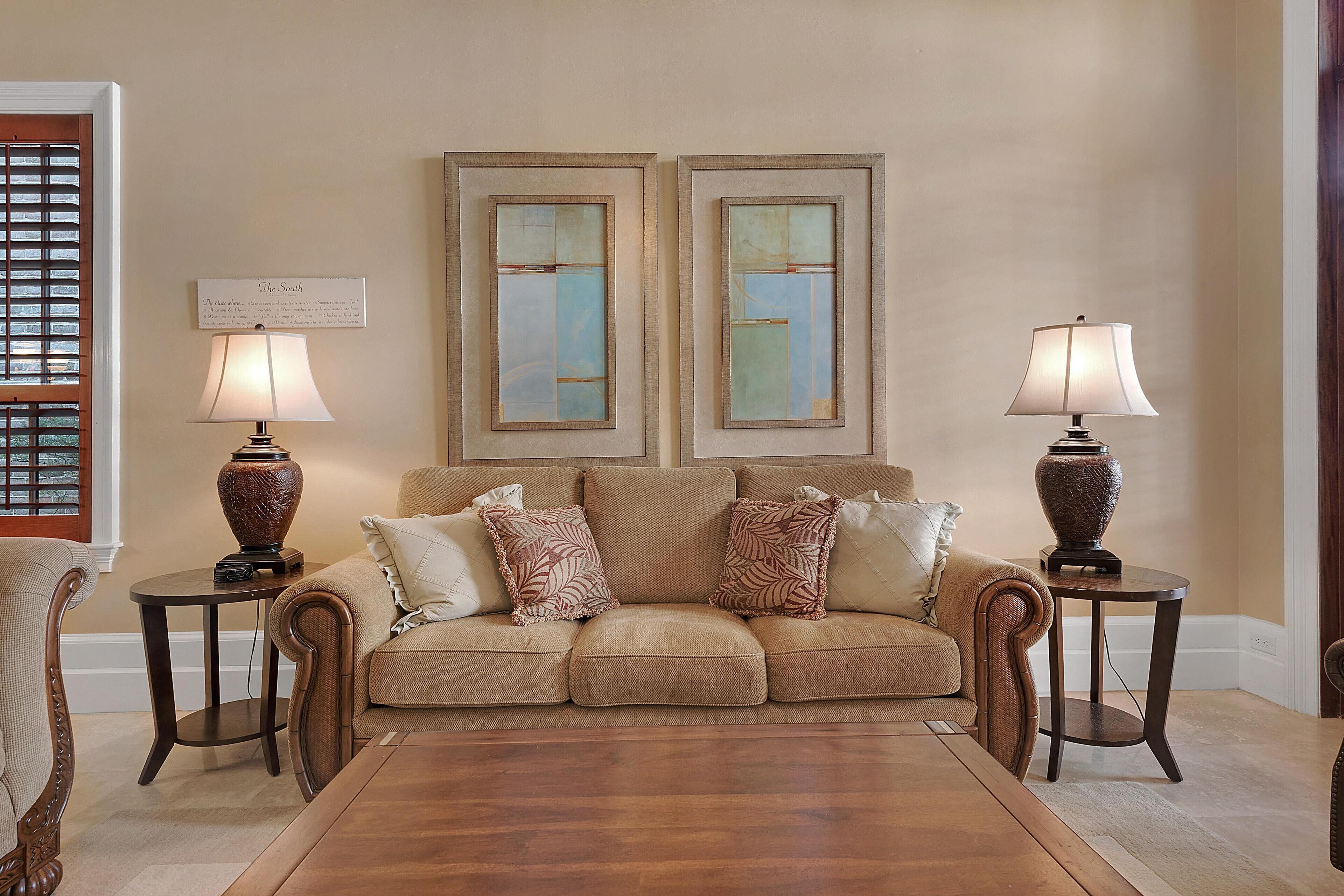 Ein Wohnzimmer mit einem beigefarbenen Sofa, zwei Nachttischen mit Lampen und zwei gerahmten abstrakten Bildern an der Wand.