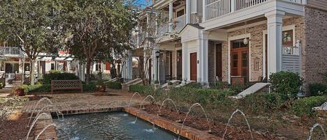 A courtyard with a water feature, brick pathway, and a building with a balcony and multiple windows.