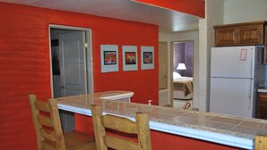 Una cocina con pared roja, refrigerador blanco y mesa de madera con dos sillas.