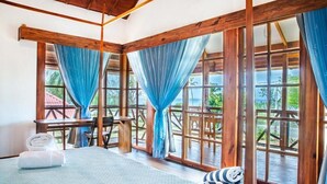 A room with a bed, a table, and chairs, large windows with curtains, and a view of greenery outside. - Miraflores Boutique Hotel (San Andrés)