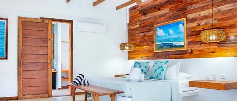 Un dormitorio con techo de madera, una cama con colchón blanco, un banco de madera y una estantería de pared.