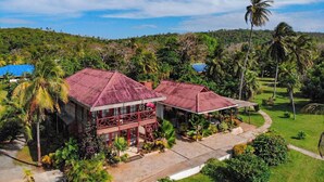 A two-story building with a red roof, surrounded by lush greenery and palm trees. - Miraflores Boutique Hotel (San Andrés)