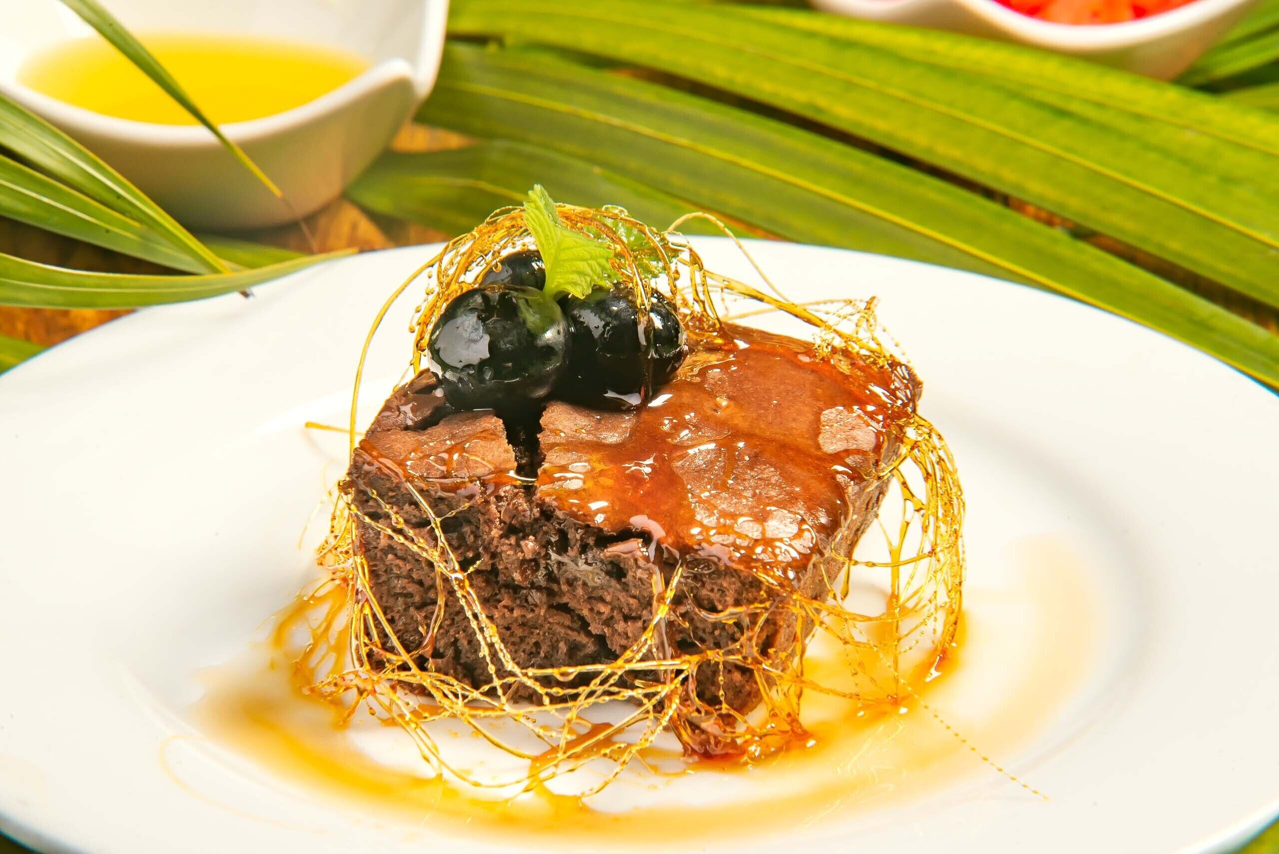 Un dessert servi dans une assiette blanche, nappé d’une sauce et agrémenté d’une garniture.