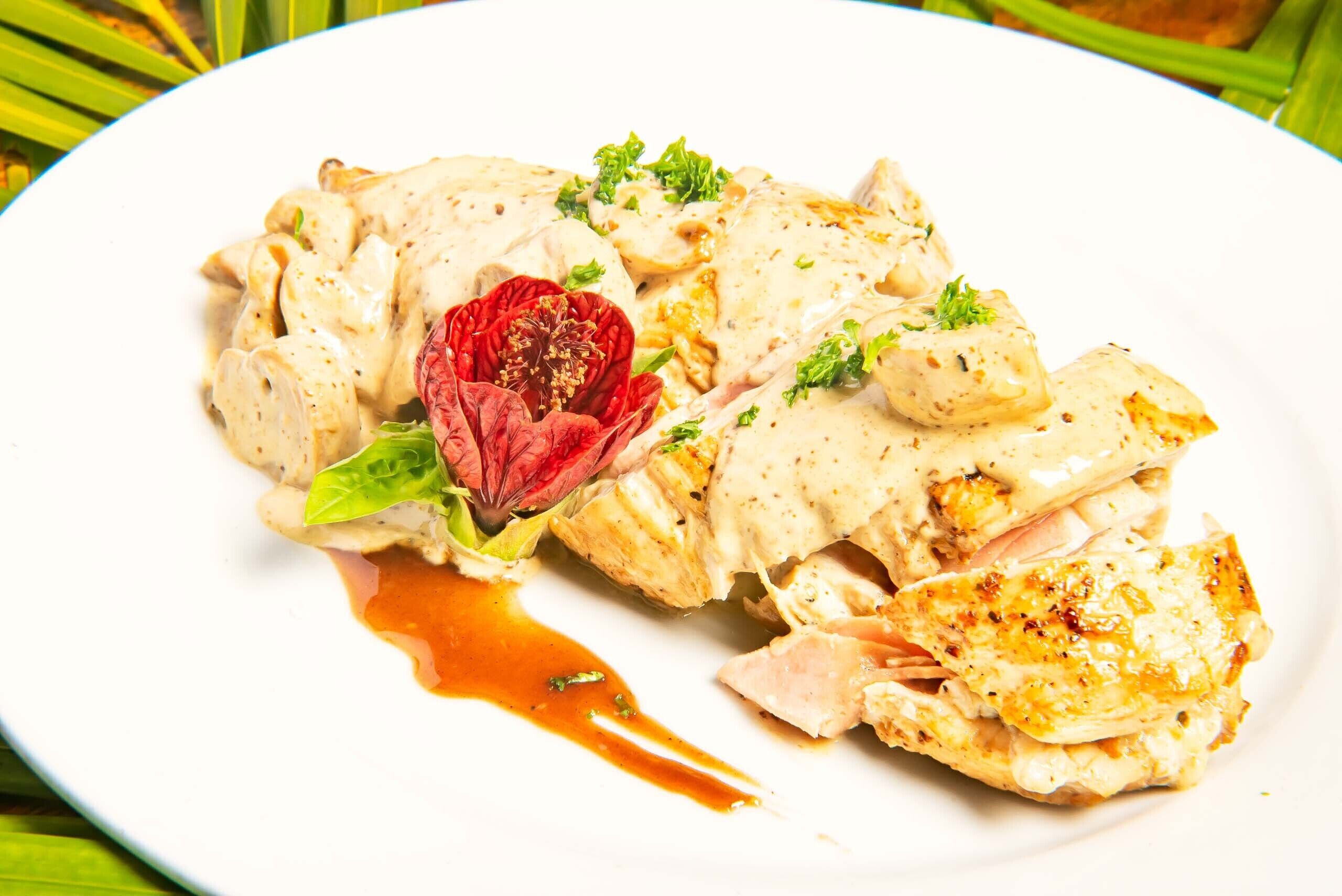A plate of food with a creamy sauce, garnished with herbs and a red flower.