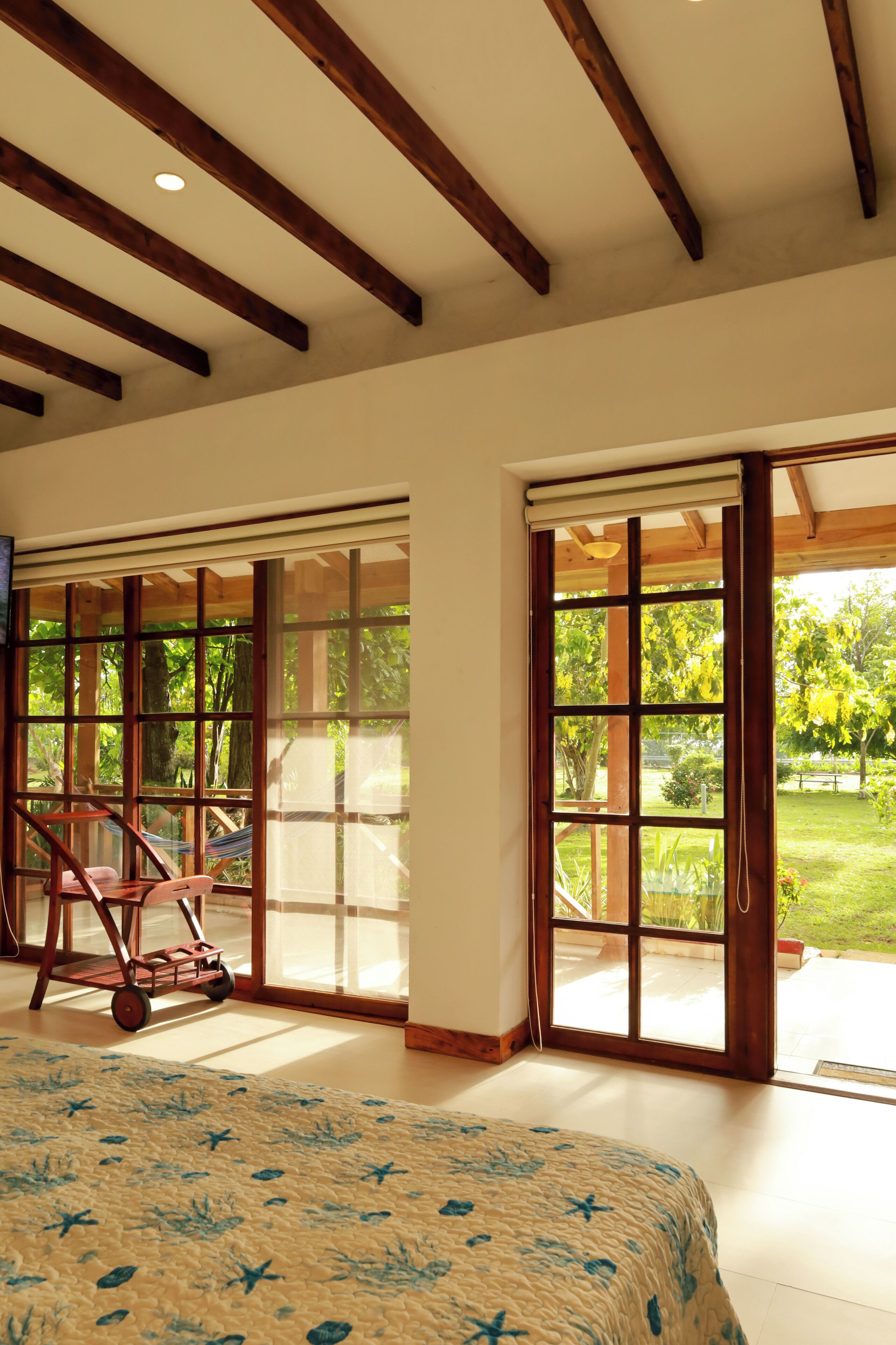 Una habitación amplia con una cama grande, vigas de madera en el techo y vistas a un jardín a través de puertas corredizas de vidrio.