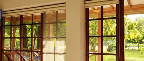 Una habitación amplia con una cama grande, vigas de madera en el techo y vistas a un jardín a través de puertas corredizas de vidrio.